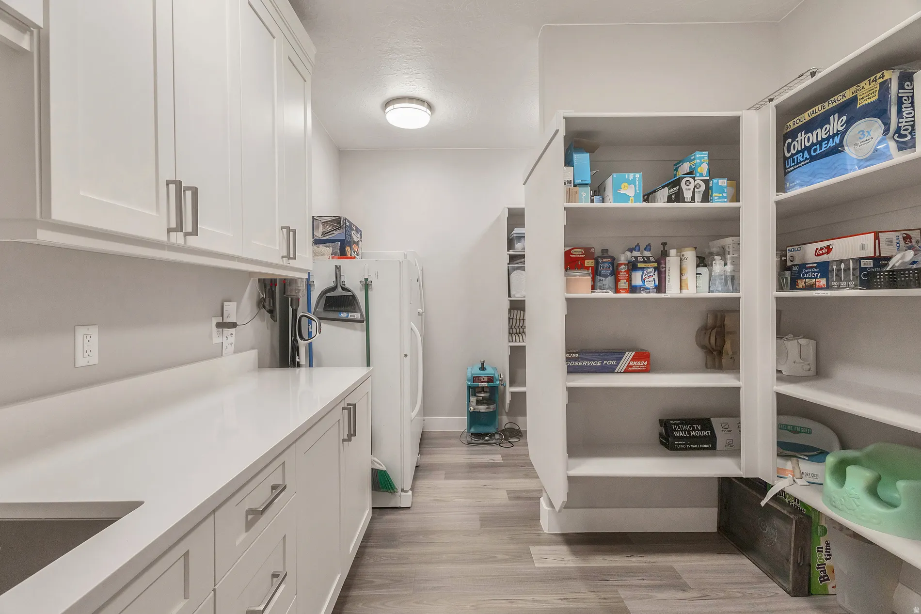 White cabinetry with brushed nickel hardware, expansive countertop space, integrated sink, recessed lighting, and wood-finish flooring