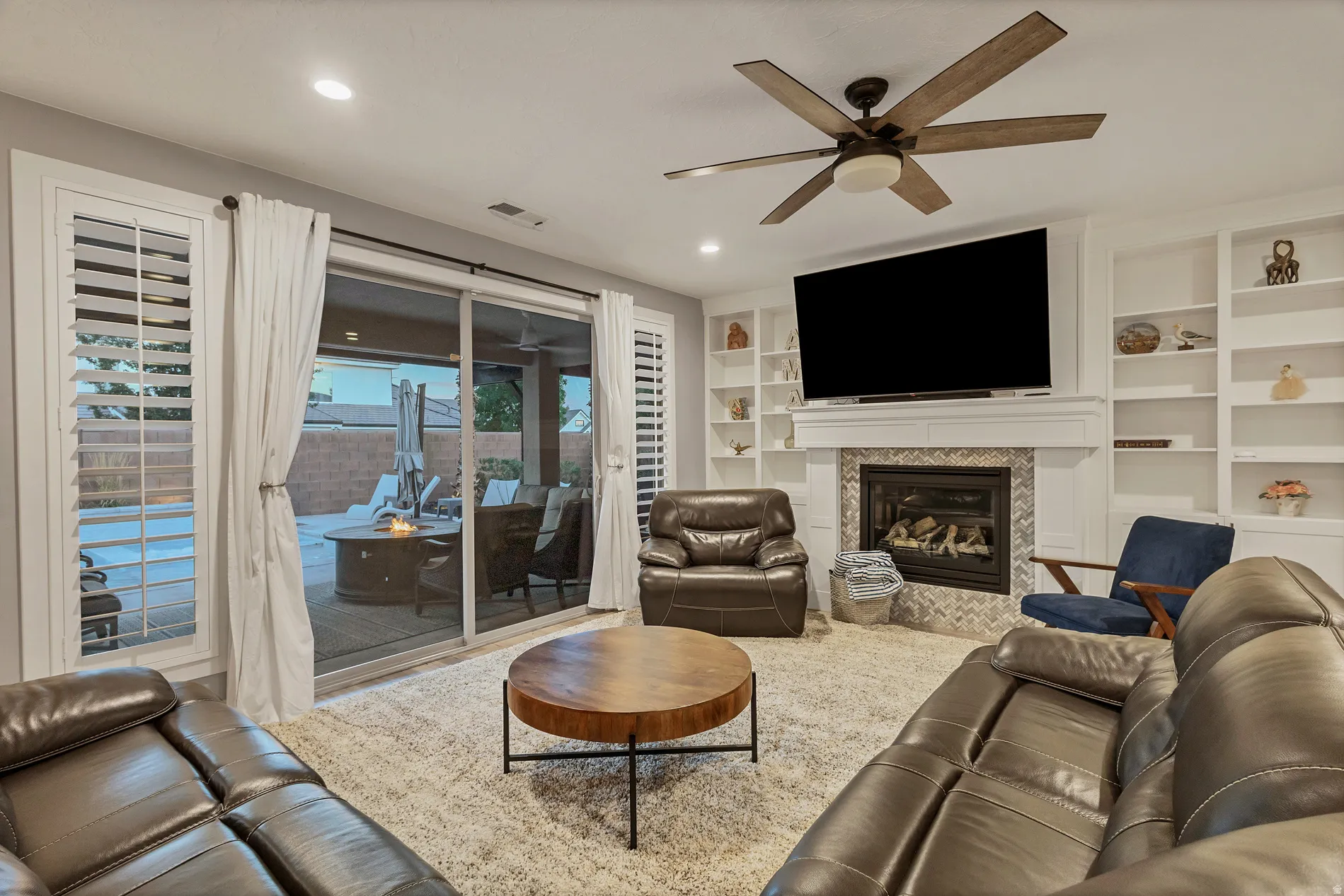 Built-in shelving flanking a gas fireplace with a tiled surround, a ceiling fan, and large sliding glass doors leading to an outdoor area