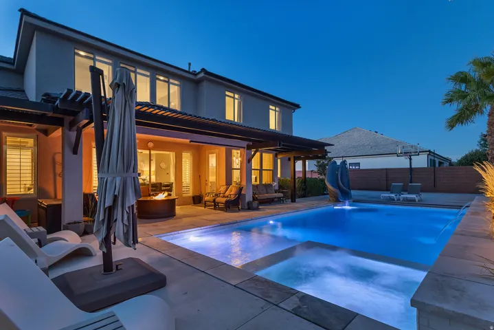 Expansive rear patio featuring a built-in swimming pool with an integrated spa, an overhead pergola, and a circular fire pit