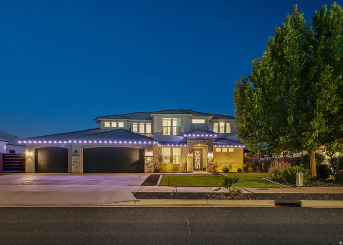Stucco exterior with stone accents, multiple windows, attached two-car garage, manicured lawn, and mature tree landscaping
