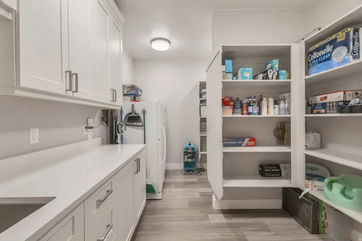 White cabinetry with brushed nickel hardware, expansive countertop space, integrated sink, recessed lighting, and wood-finish flooring