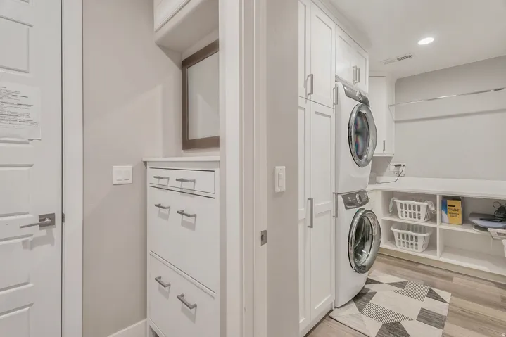 Laundry area featuring wood-finish flooring, white cabinetry, integrated shelving, and a stacked washer and dryer