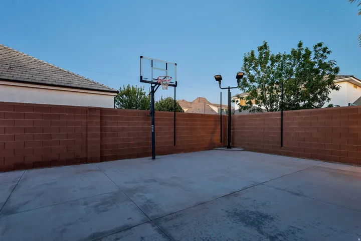 Concrete paved area featuring a basketball hoop, perimeter block wall, and integrated outdoor lighting