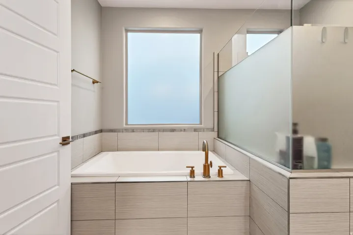 Built-in soaking tub with bronze fixtures, textured tile surround, and an adjacent frosted glass shower enclosure