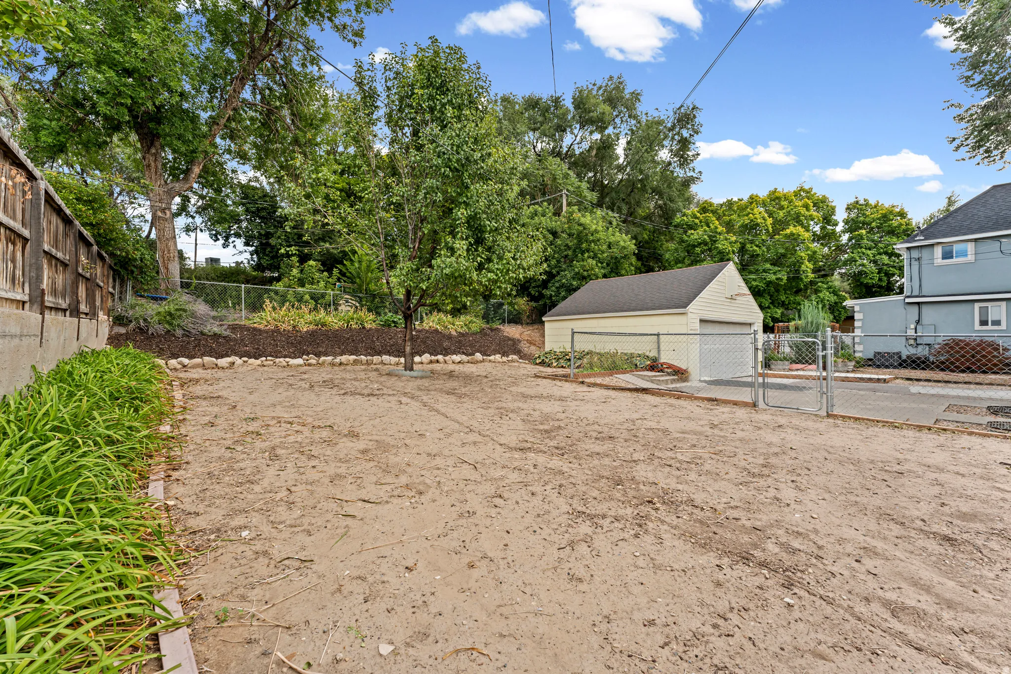 Detached garage with chain-link fencing, mature trees, wood privacy fencing, and landscaping elements