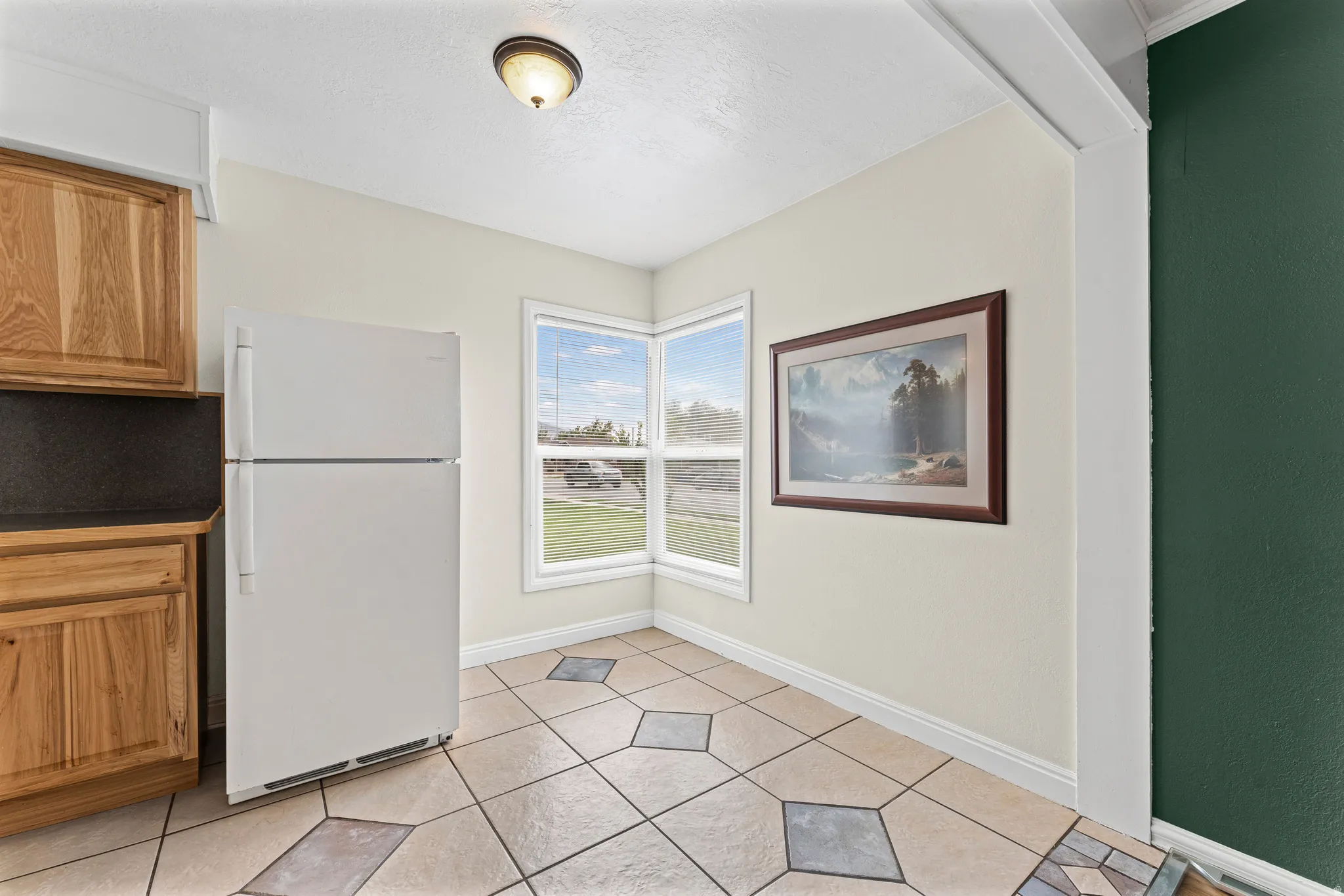 Corner windows, tile flooring with geometric accents, wood-finish cabinetry, and a flush-mount ceiling light