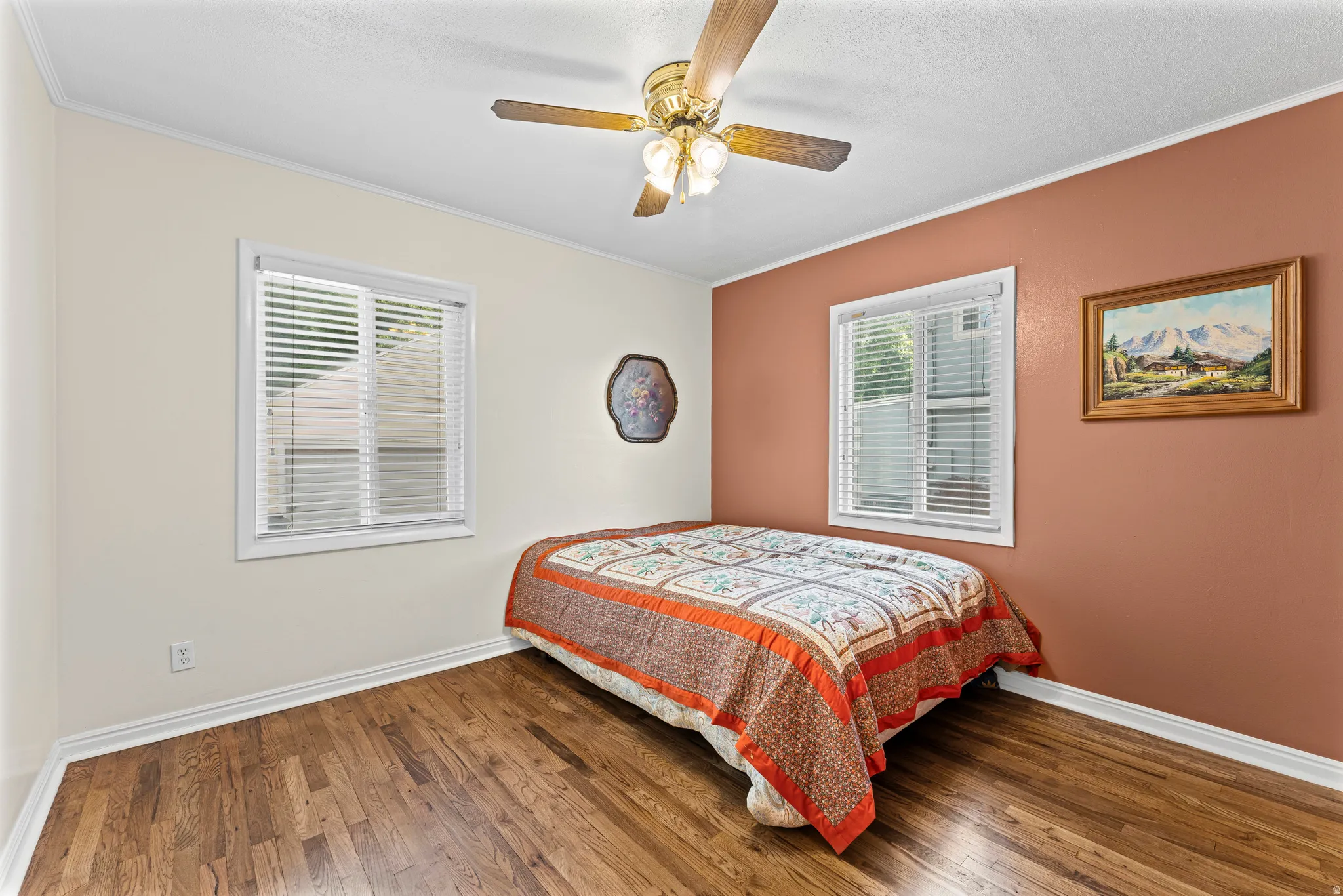 Wood-finish flooring, two windows with blinds, ceiling fan with integrated lighting, and crown molding