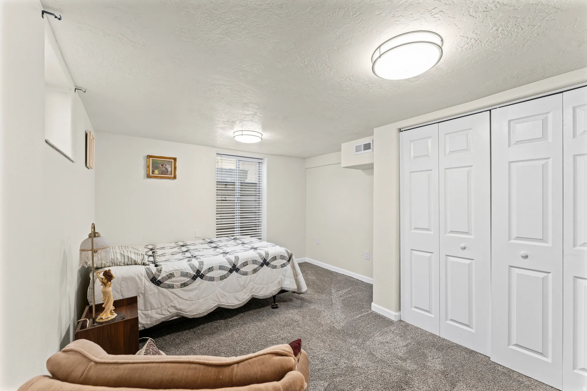 Carpeted room featuring white bi-fold closet doors, a window with blinds, and flush-mount ceiling lighting