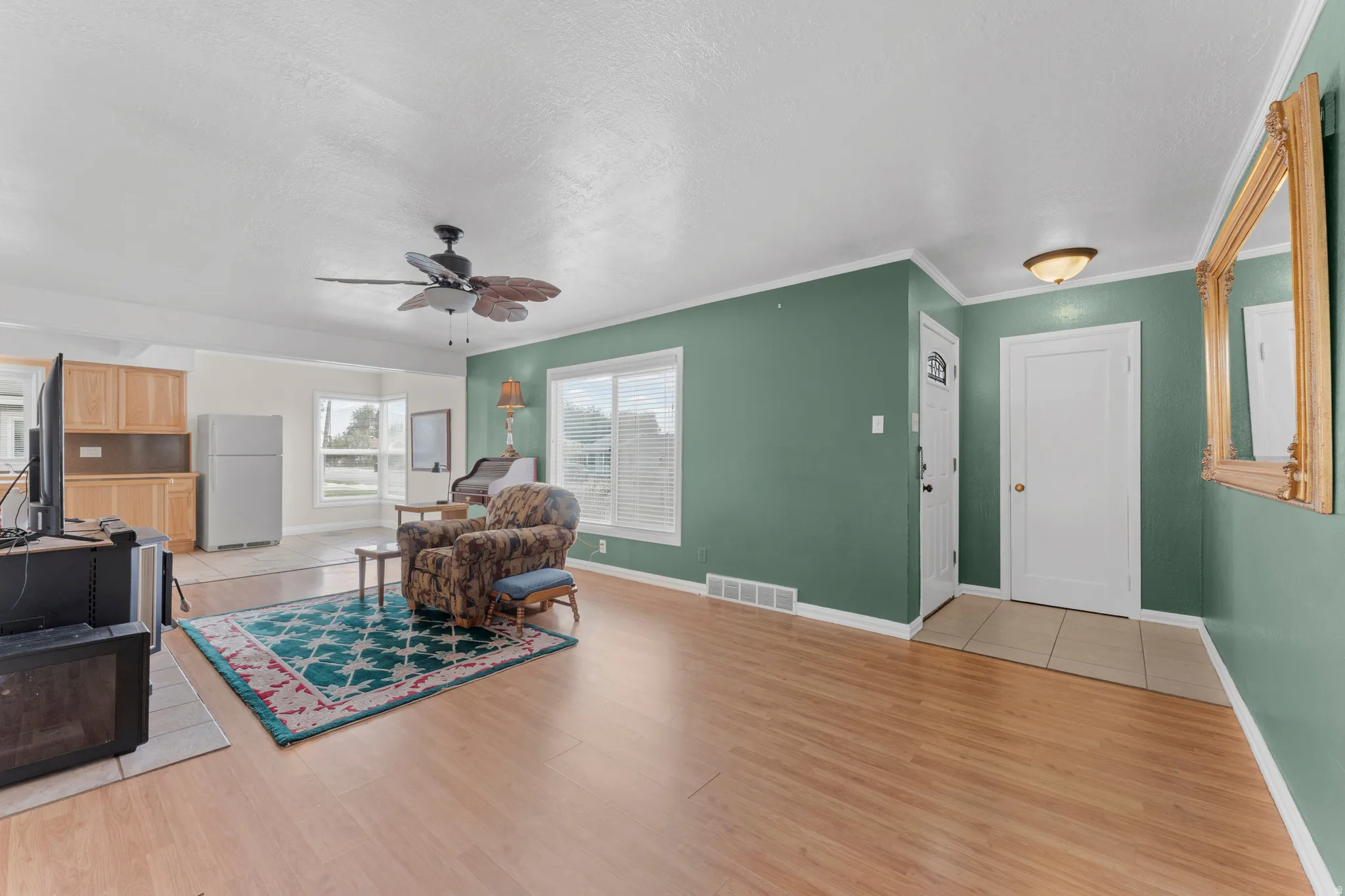 Hardwood-finish flooring, ceiling fan with integrated lighting, multiple windows with blinds, and a tiled entryway
