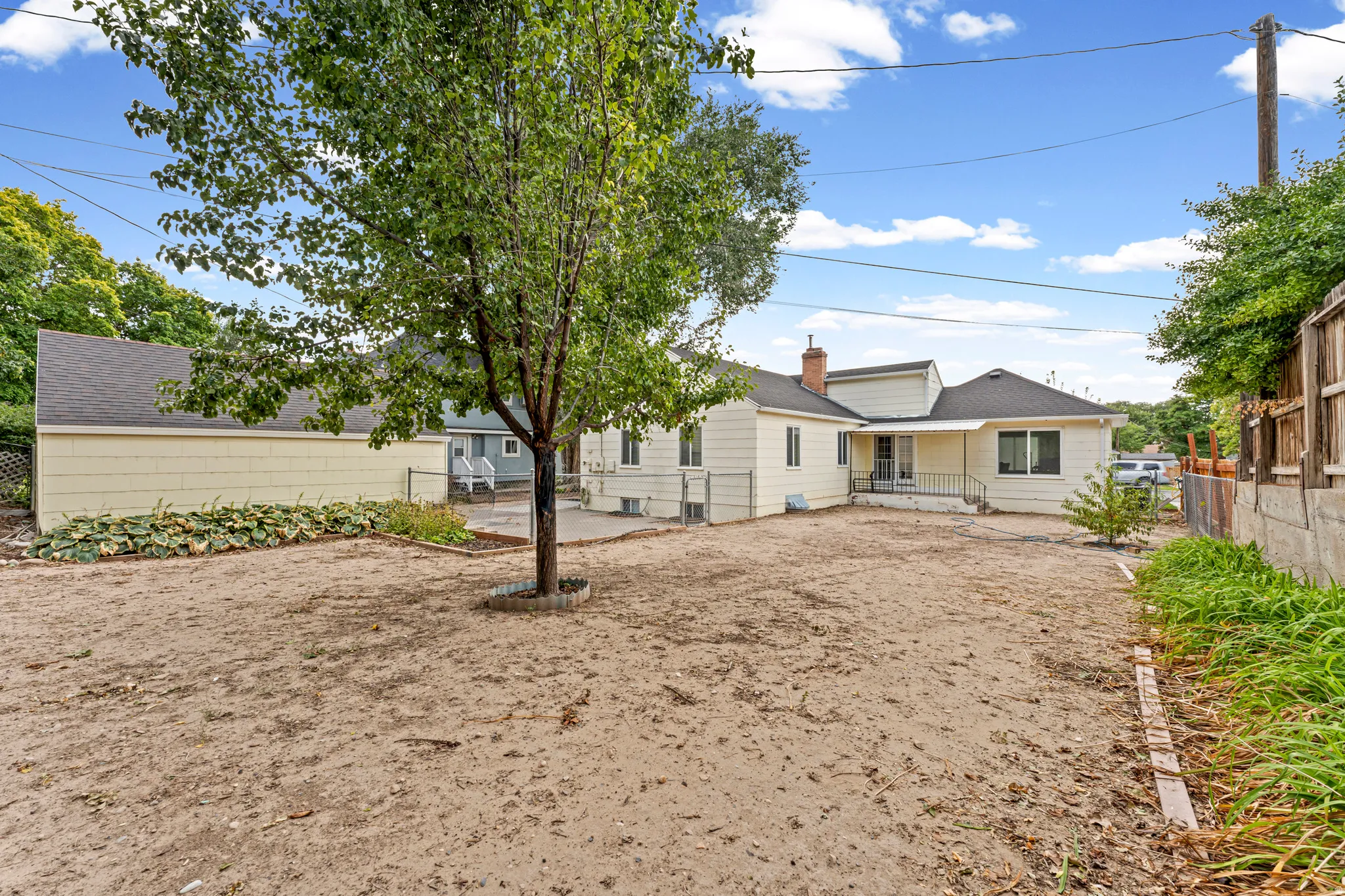 Expansive rear yard with mature trees, detached garage, and a covered patio area