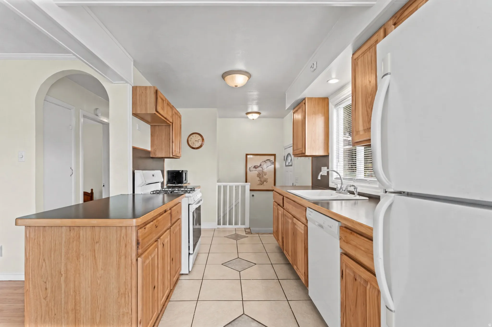Kitchen featuring wood cabinetry, dark countertops, white appliances, and a tiled floor