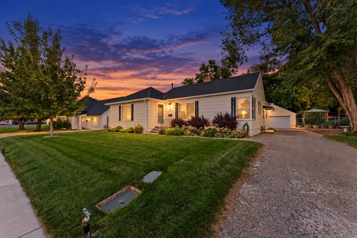 White siding exterior with black shutters, mature landscaping, paved driveway, and detached garage