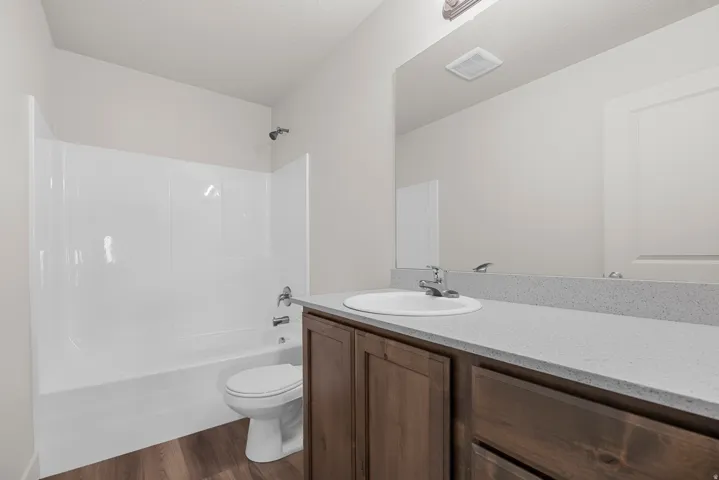 Integrated tub and shower combination, wood-finish vanity with storage, single basin sink, and a spacious vanity mirror