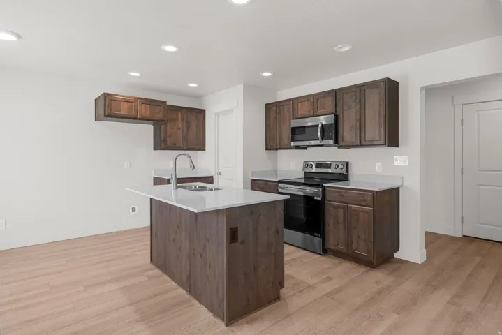 Kitchen featuring wood-finish flooring, dark wood cabinetry, light-toned countertops, and stainless steel appliances