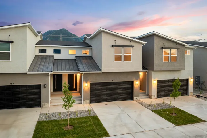 Modern townhome architecture featuring a light gray exterior, dark garage doors, and a metal roof accent