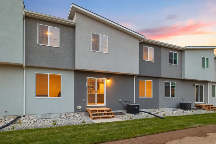 Multi-level stucco exterior with multiple windows and sliding glass doors, featuring a grass lawn and rock landscaping