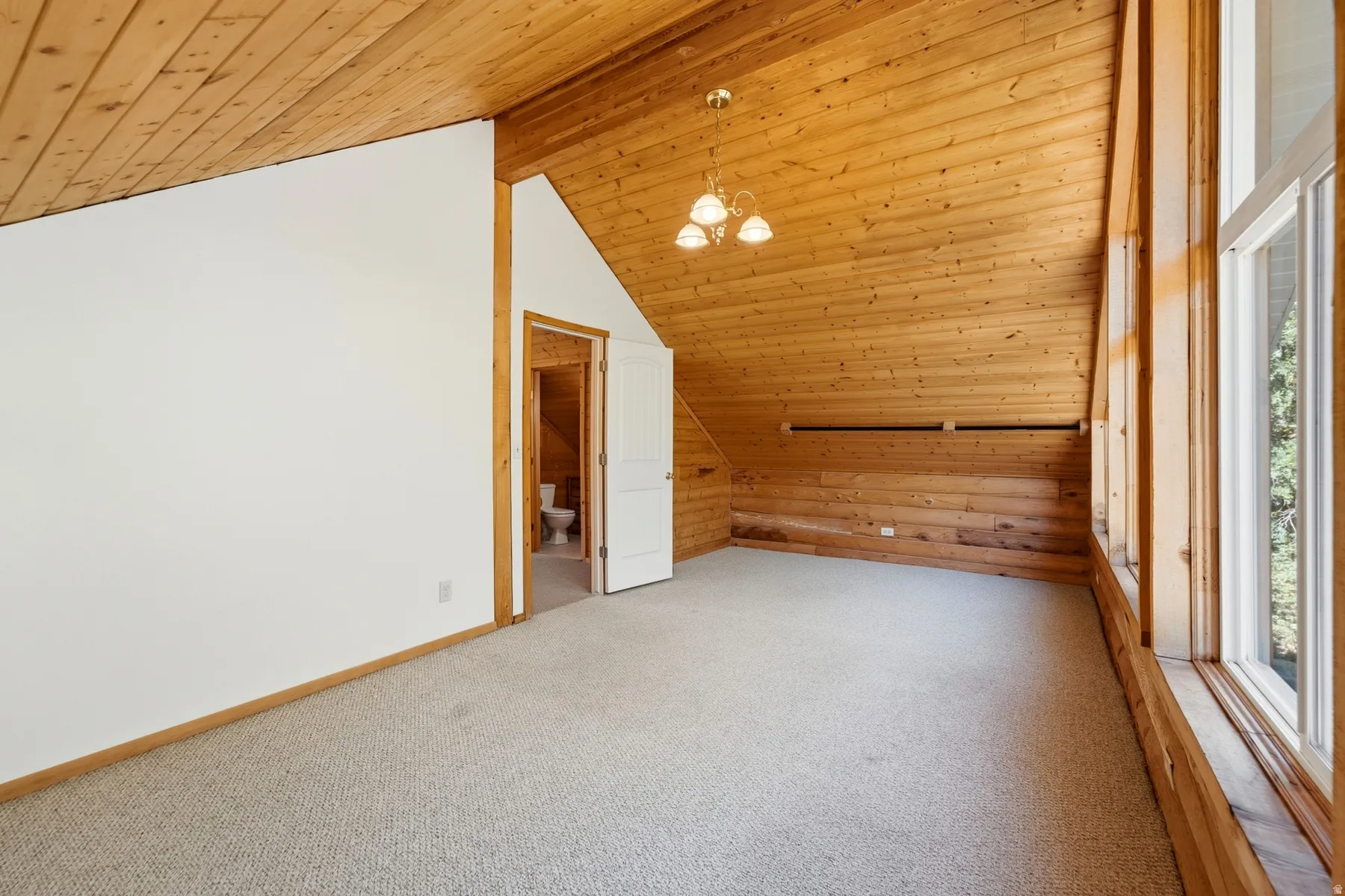 Vaulted wood-paneled ceiling with a three-light chandelier, full-height windows, and wall-to-wall carpeting