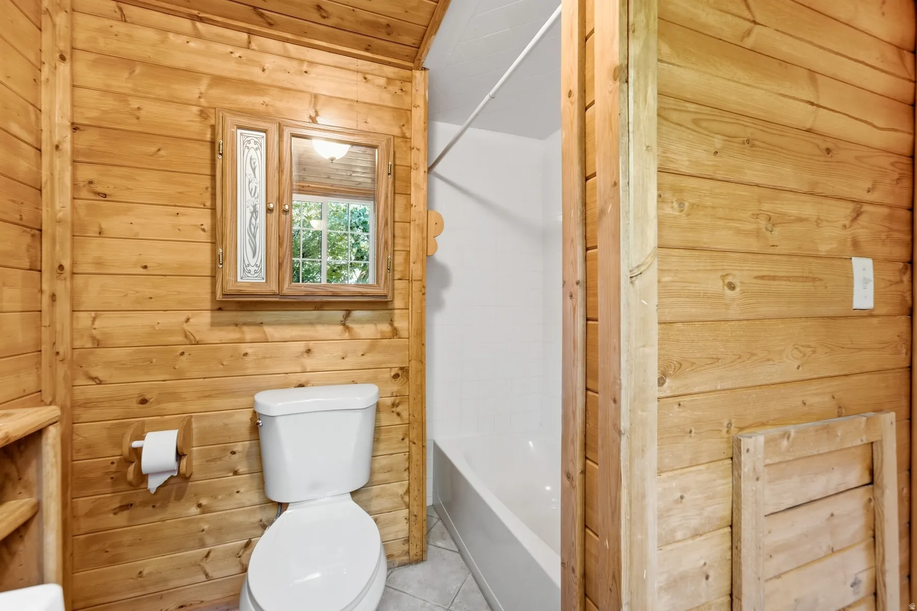 Bathroom featuring wood paneling, a white toilet, a built-in medicine cabinet with decorative glass, and a white bathtub
