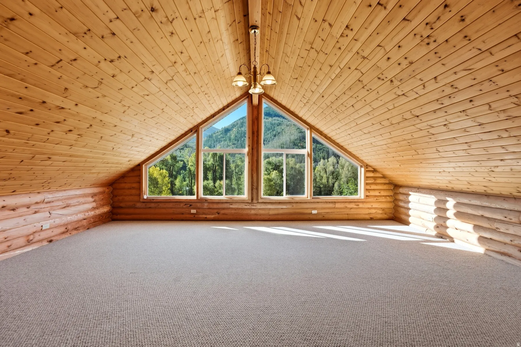 Vaulted wooden plank ceiling, log-style wall construction, triangular window framing, dual hanging light fixture, and carpeting