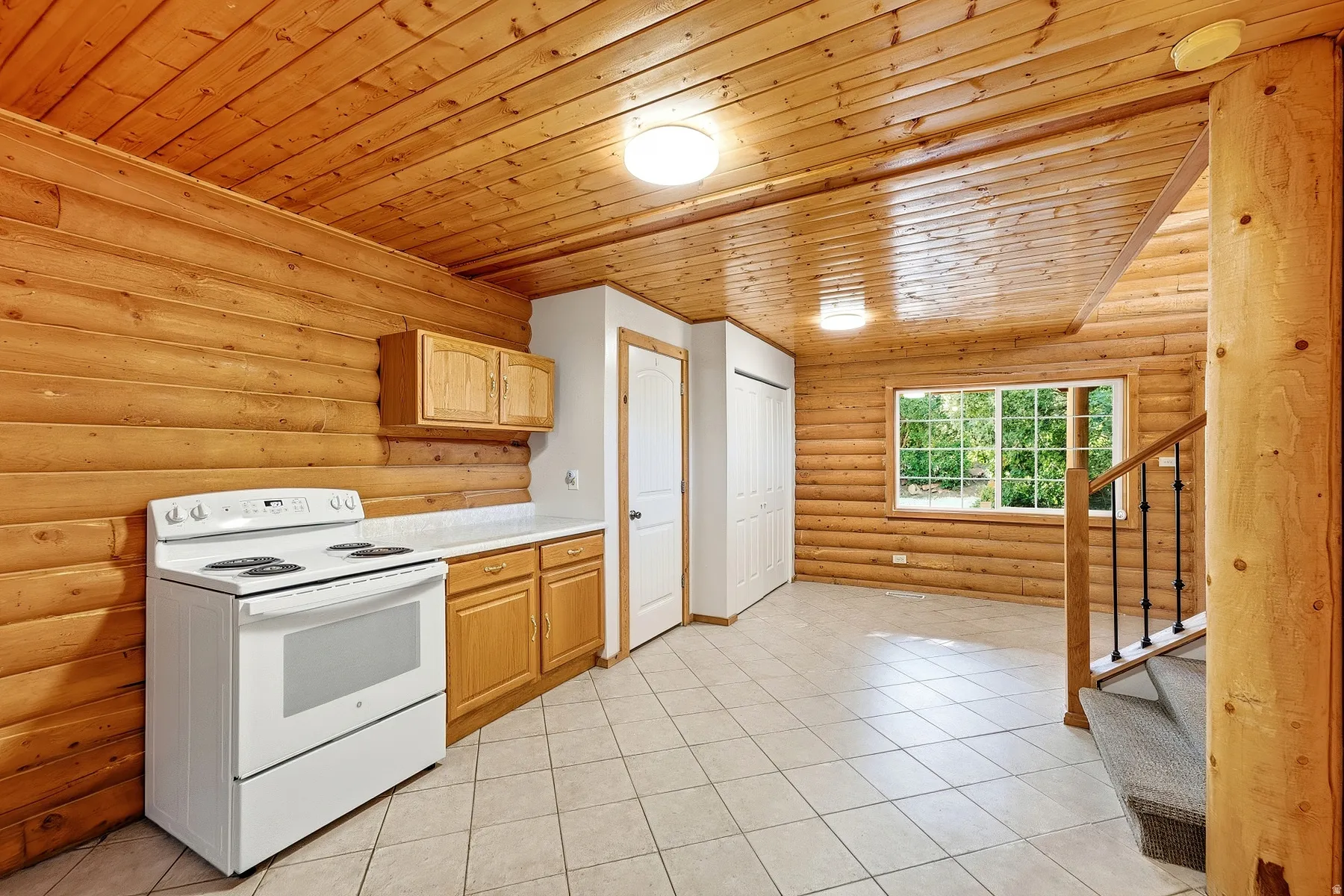 Wood plank walls and ceiling, white tile flooring, wood cabinetry, white countertop, and window with exterior exposure