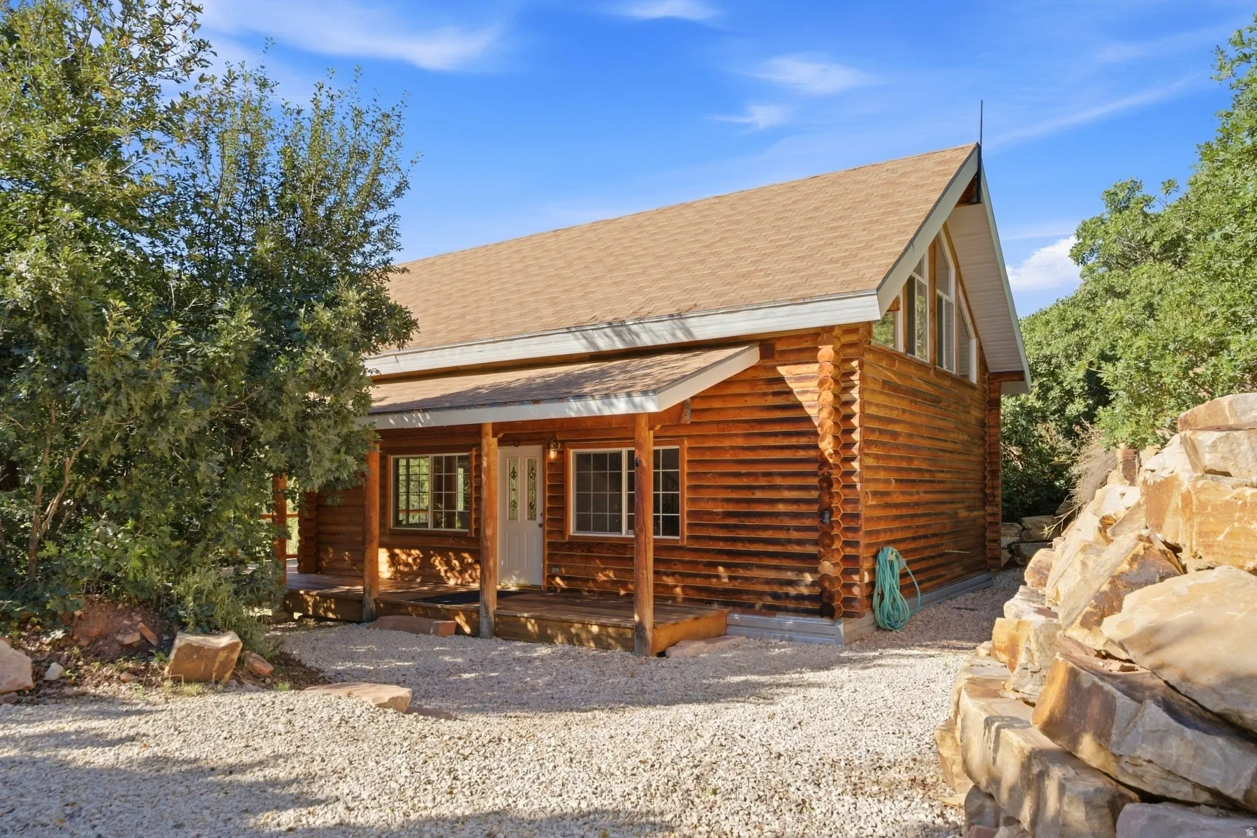 Wood-sided residence featuring a covered porch, an A-frame roofline, and natural rock landscaping