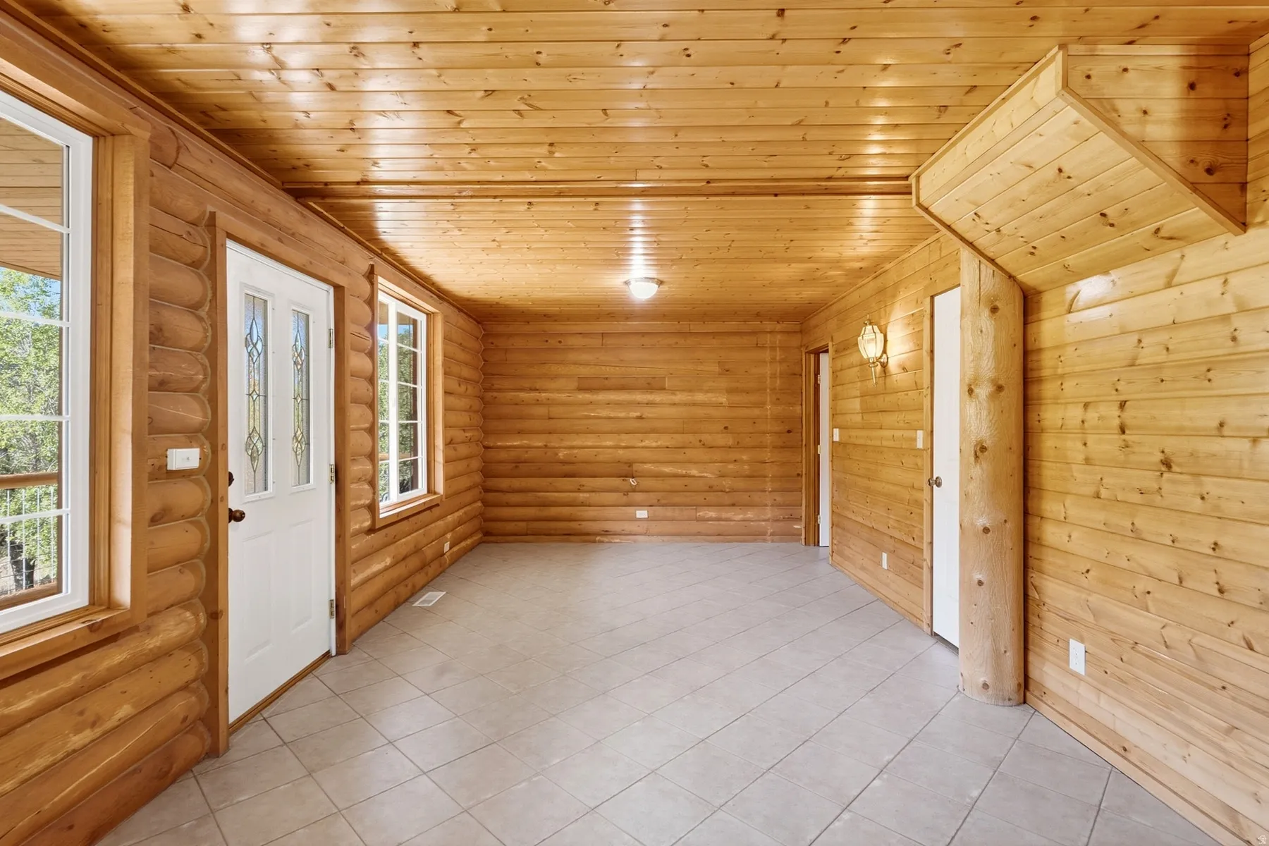 Wood-paneled walls and ceiling, white paneled doors, square tile flooring, and multiple windows