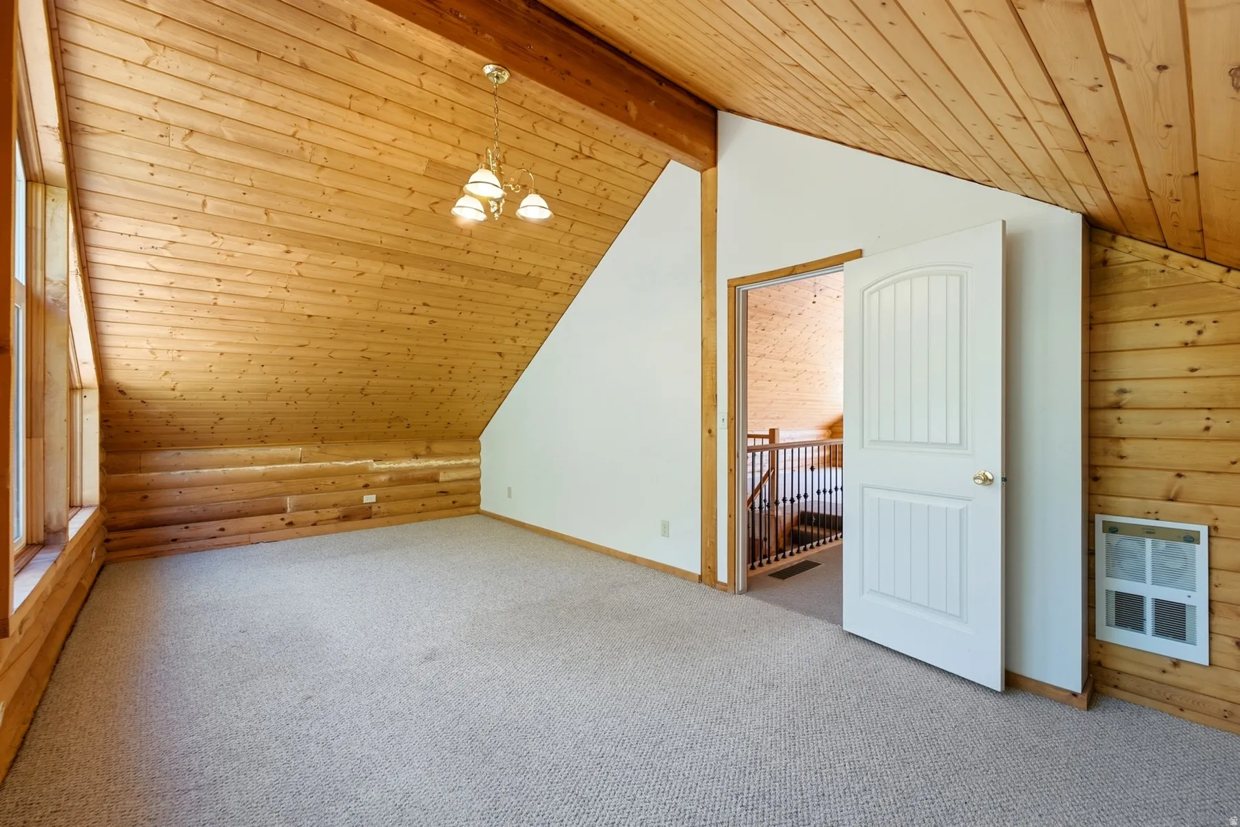 Vaulted wood-paneled ceiling with exposed beam, multiple windows, plush carpeted flooring, and a three-light chandelier