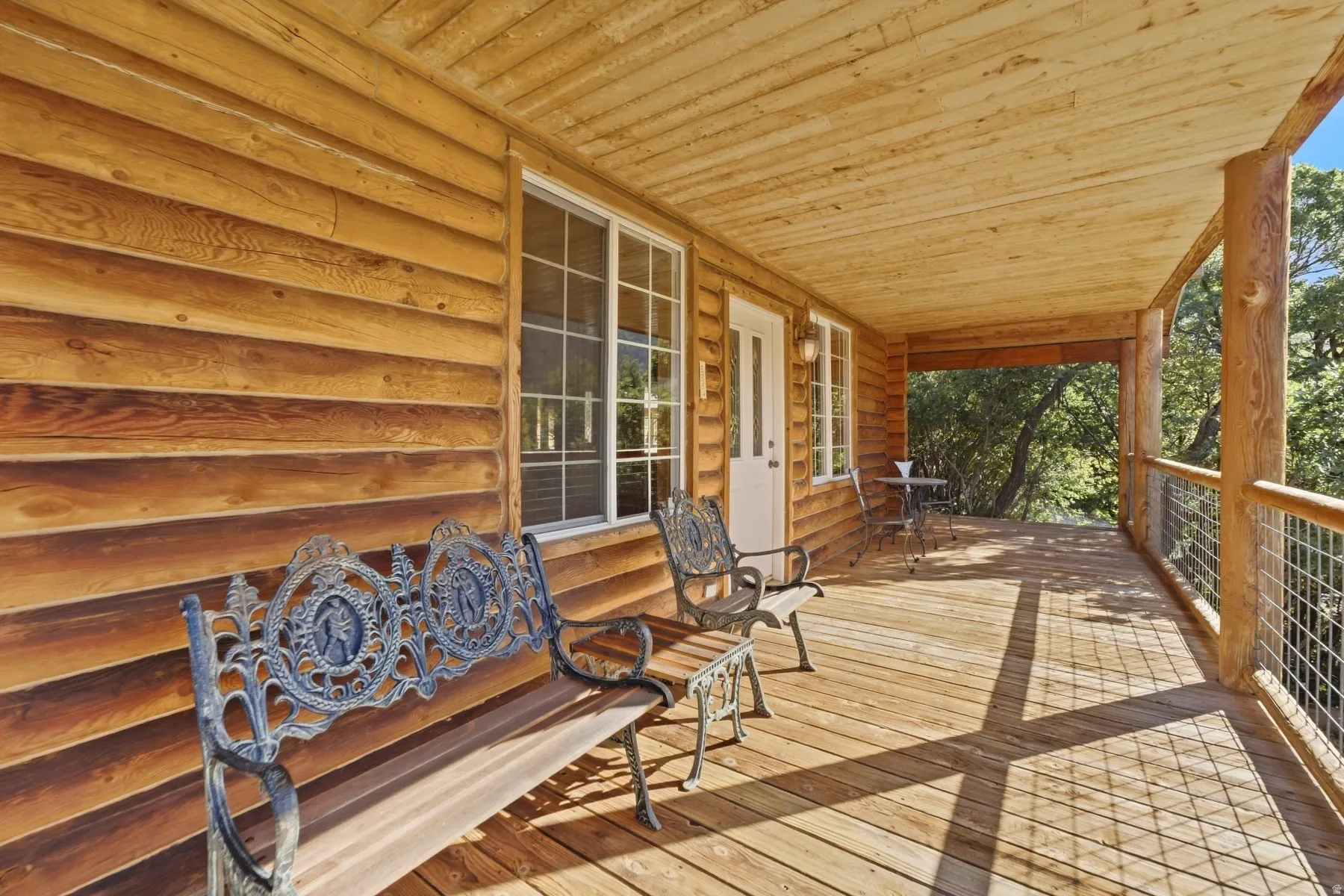 Expansive covered porch featuring natural wood siding, wood plank flooring, log support columns, and a metal mesh railing system