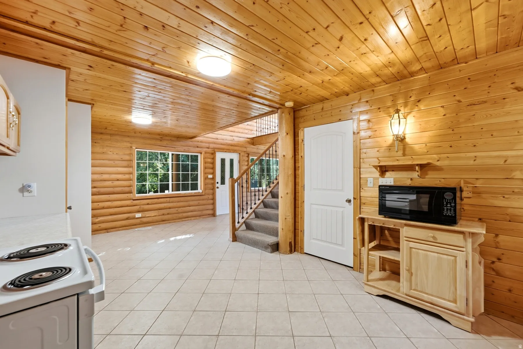 Wood-paneled walls and ceiling, tile flooring, window with exterior views, built-in stairwell, and a wooden storage cabinet