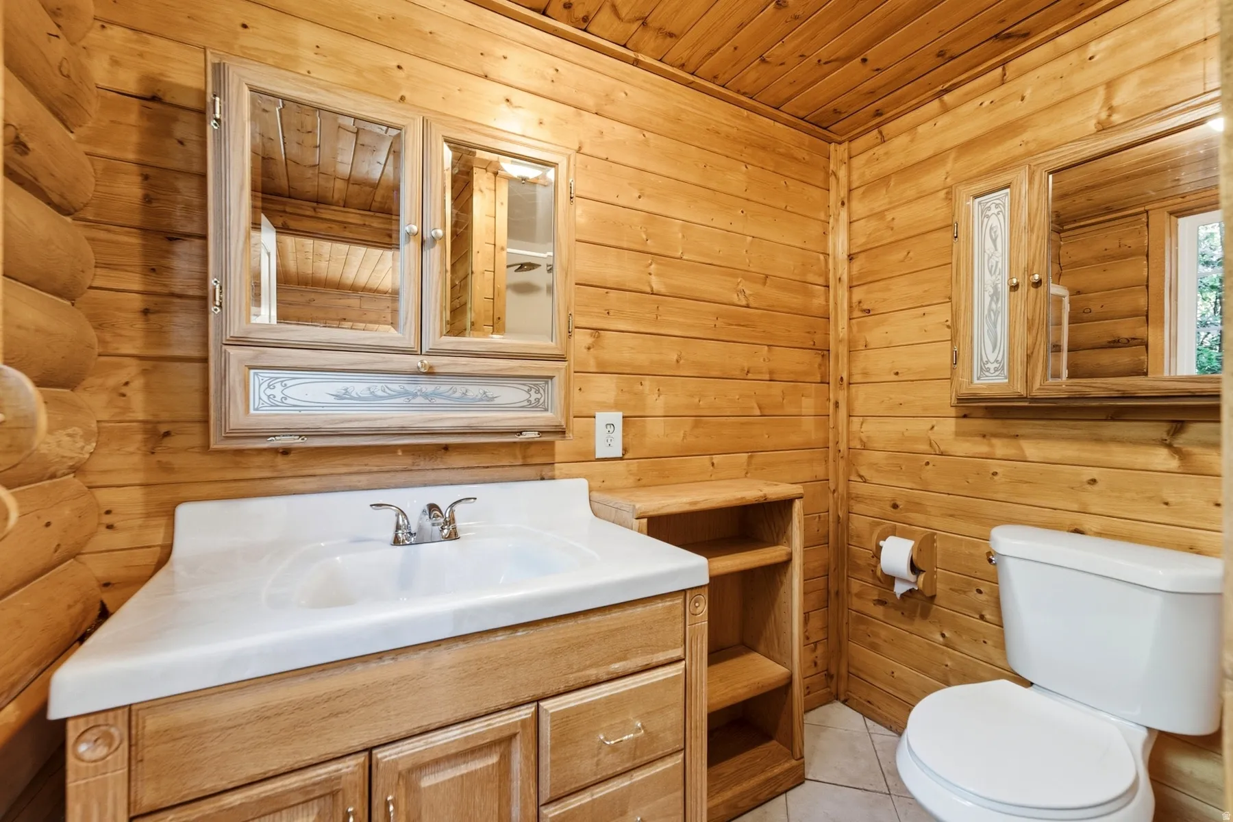 Wood-paneled walls and ceiling, wood-finish vanity with an integrated sink, built-in storage shelving, and a dual-mirror medicine cabinet