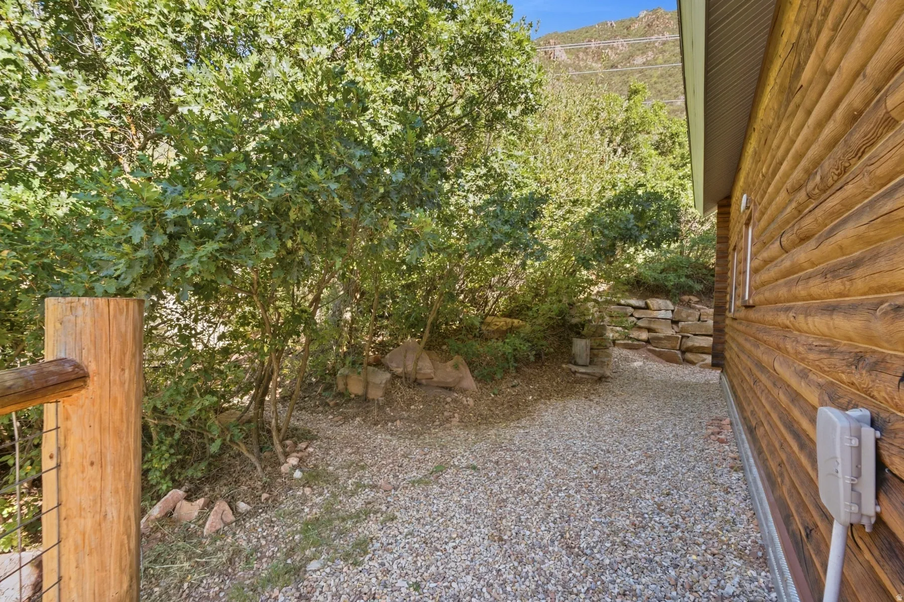 Log-style exterior siding with a natural wood finish, gravel pathway, and a natural stone retaining wall