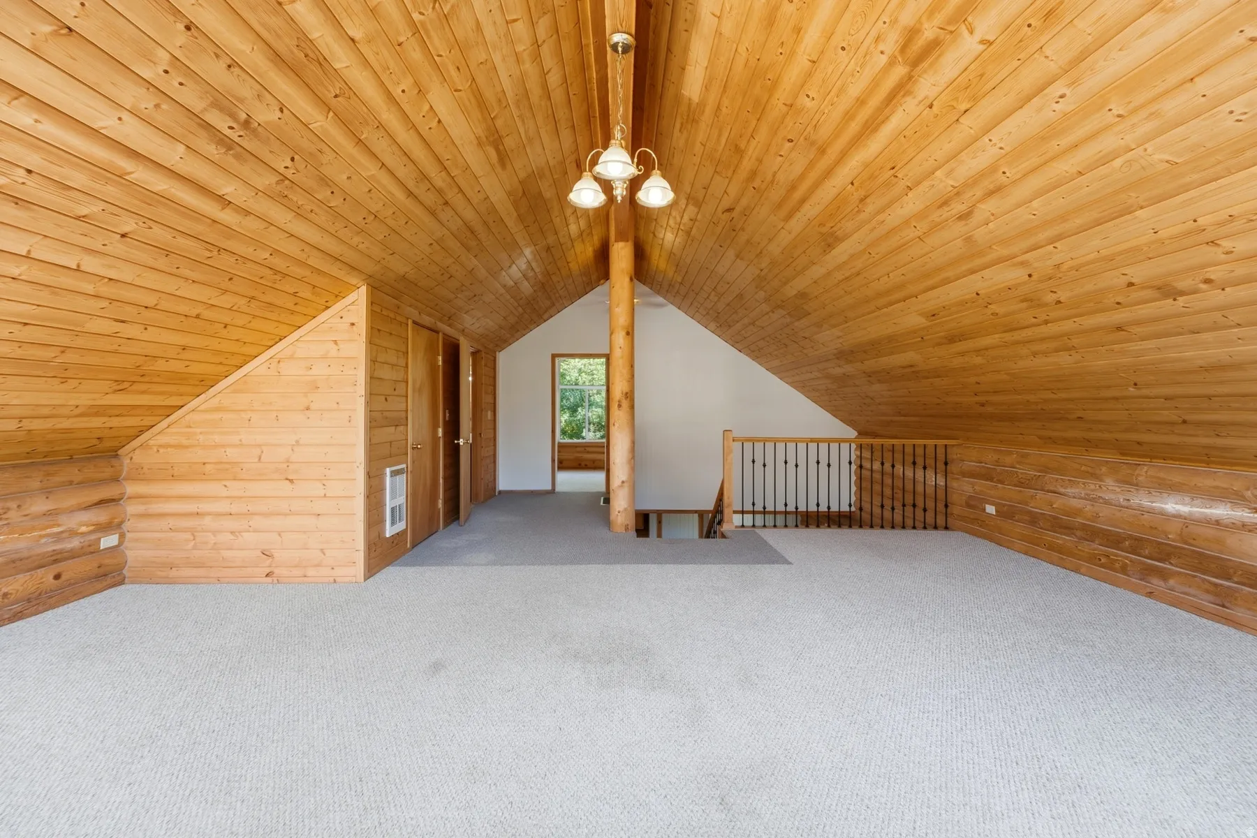 Light-colored carpeting, wood-paneled walls, vaulted wood-plank ceiling, exposed wood support beam, and a wrought iron railing