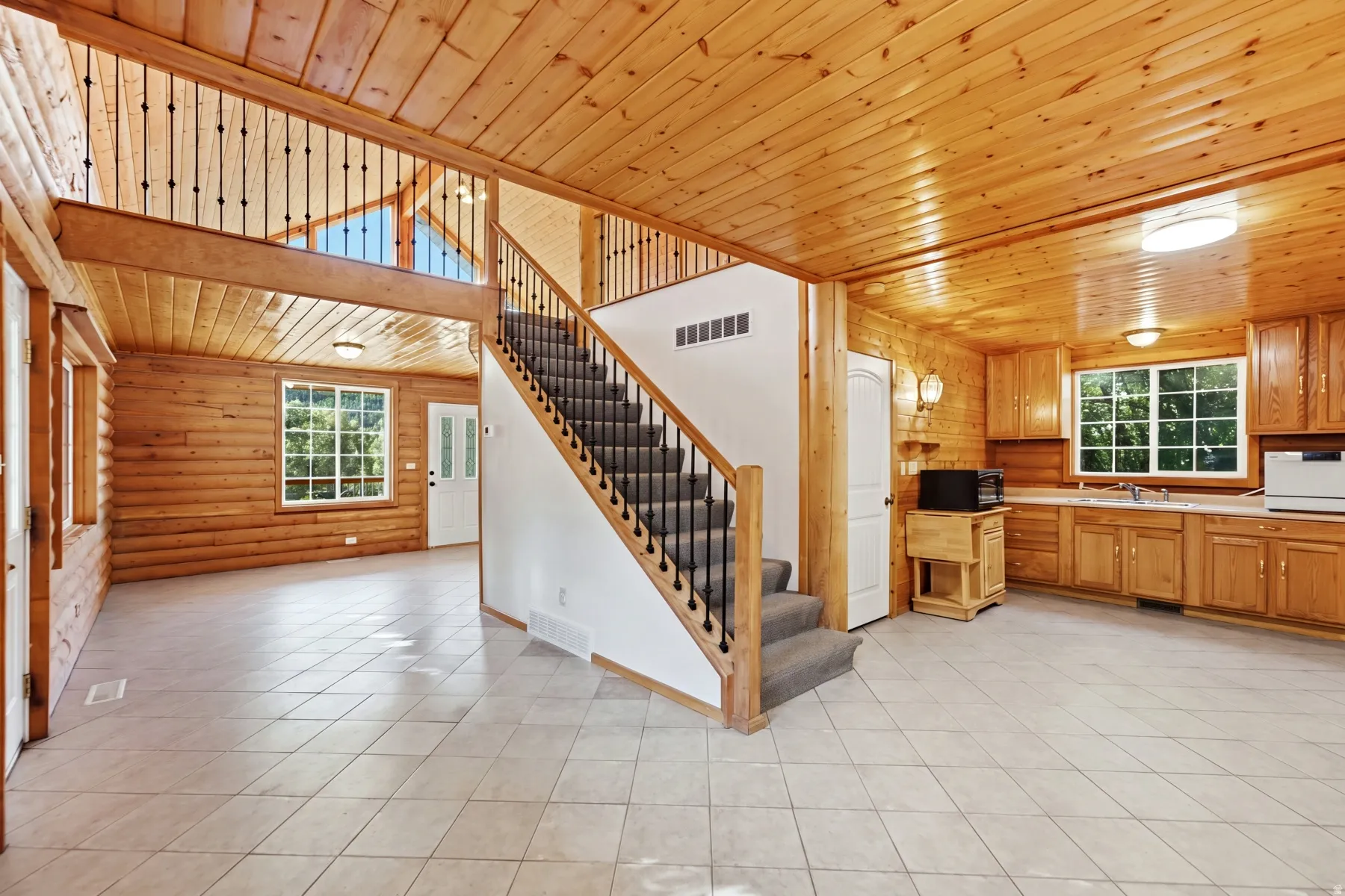 Open-concept interior featuring wood-paneled walls and ceiling, a staircase with carpeted treads and metal balusters, and light-toned tile flooring