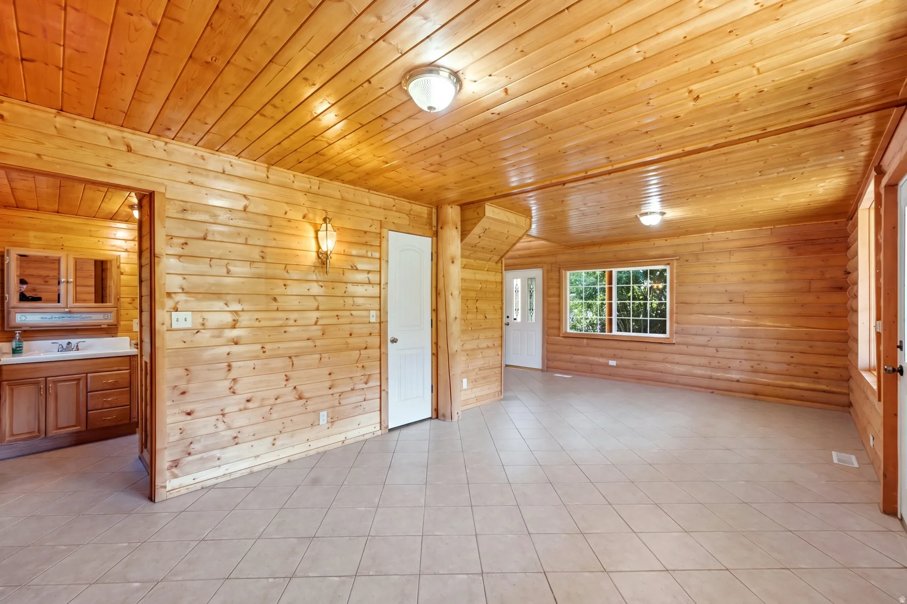 Wood-paneled walls and ceiling, recessed ceiling lighting, tile flooring, white-framed window, and a built-in bathroom vanity with an integrated sink