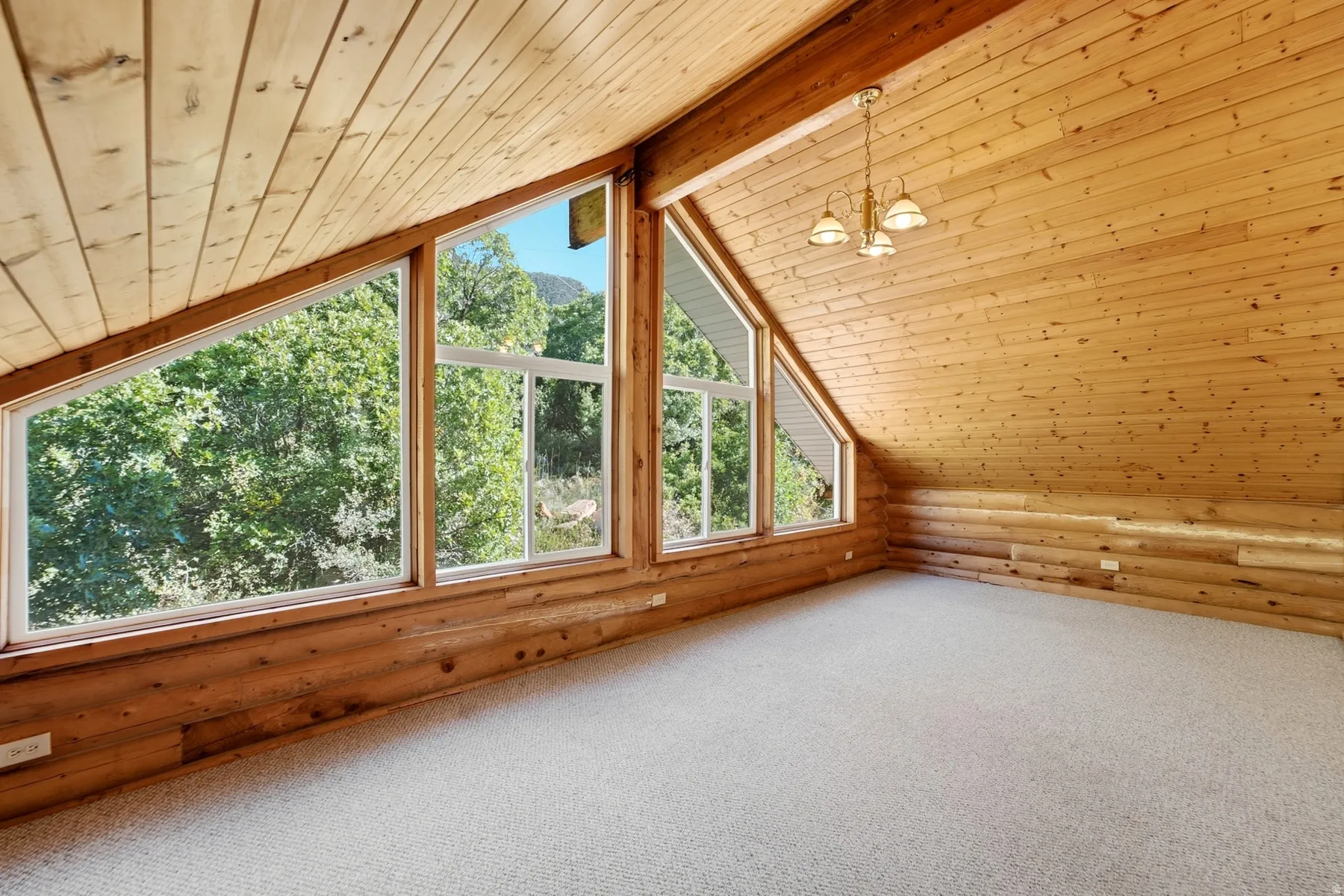 Vaulted wood-paneled ceilings, natural wood wall finishes, large picture windows, and a three-light chandelier