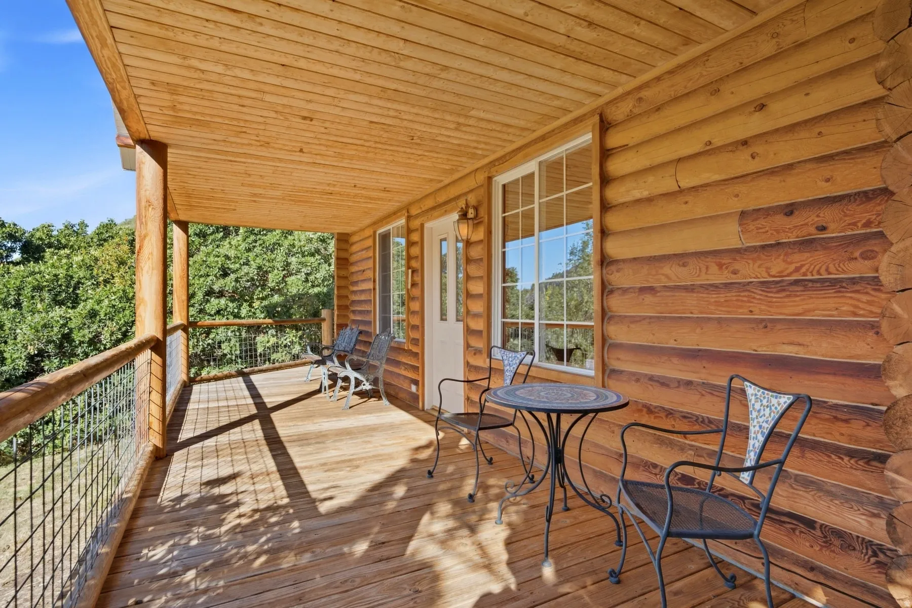Expansive wood-plank deck with a wood-plank ceiling, log siding, a white-framed window, and a white door with a window panel