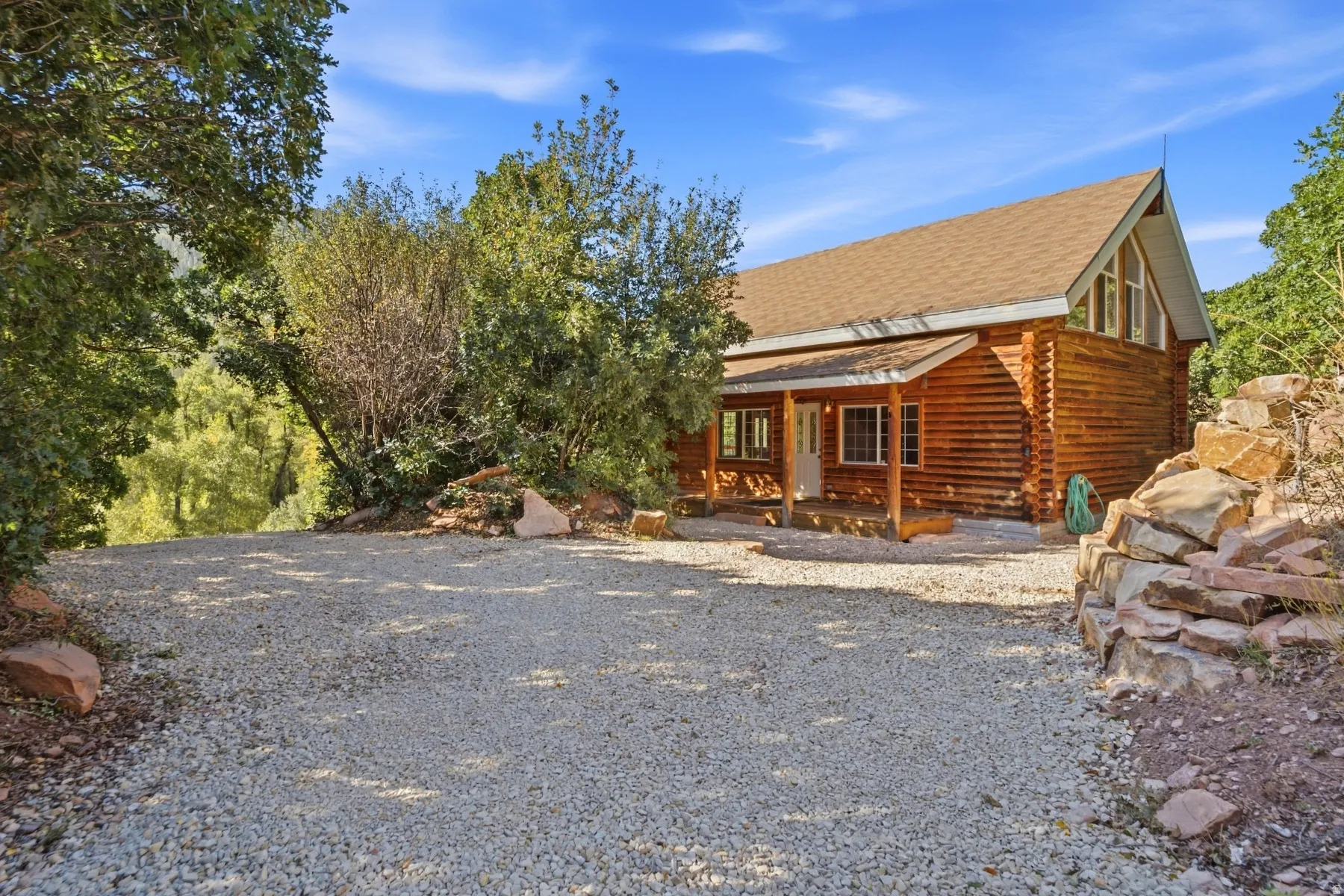 Log cabin exterior with an A-frame roofline, covered front porch, and gravel drive