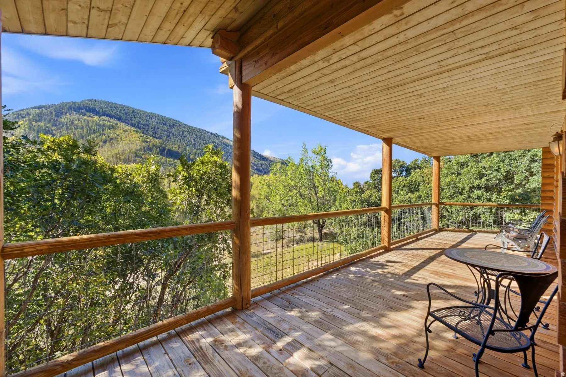Expansive wood deck with natural wood railing and wire mesh infill, featuring a wood plank ceiling and log structural columns