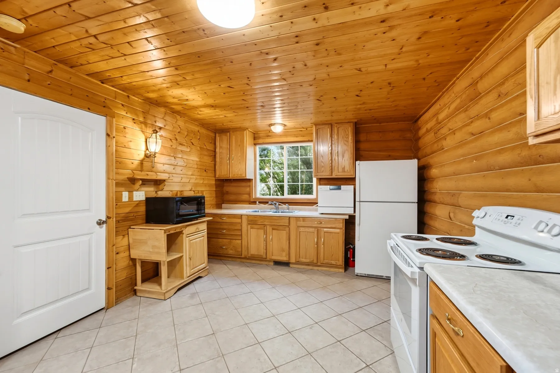Tile flooring, wood-paneled walls, wood-paneled ceiling, wood cabinetry, and a window above the sink