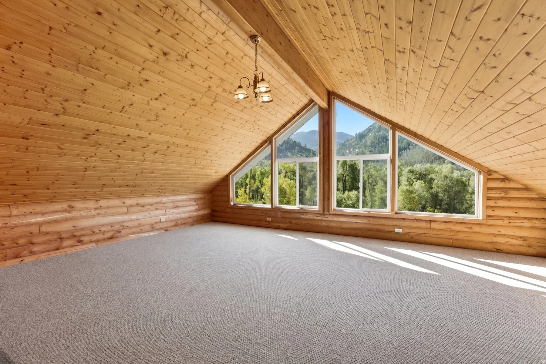 Vaulted wood-paneled ceilings, log wall accents, expansive triangular windows, recessed lighting, and neutral carpeting