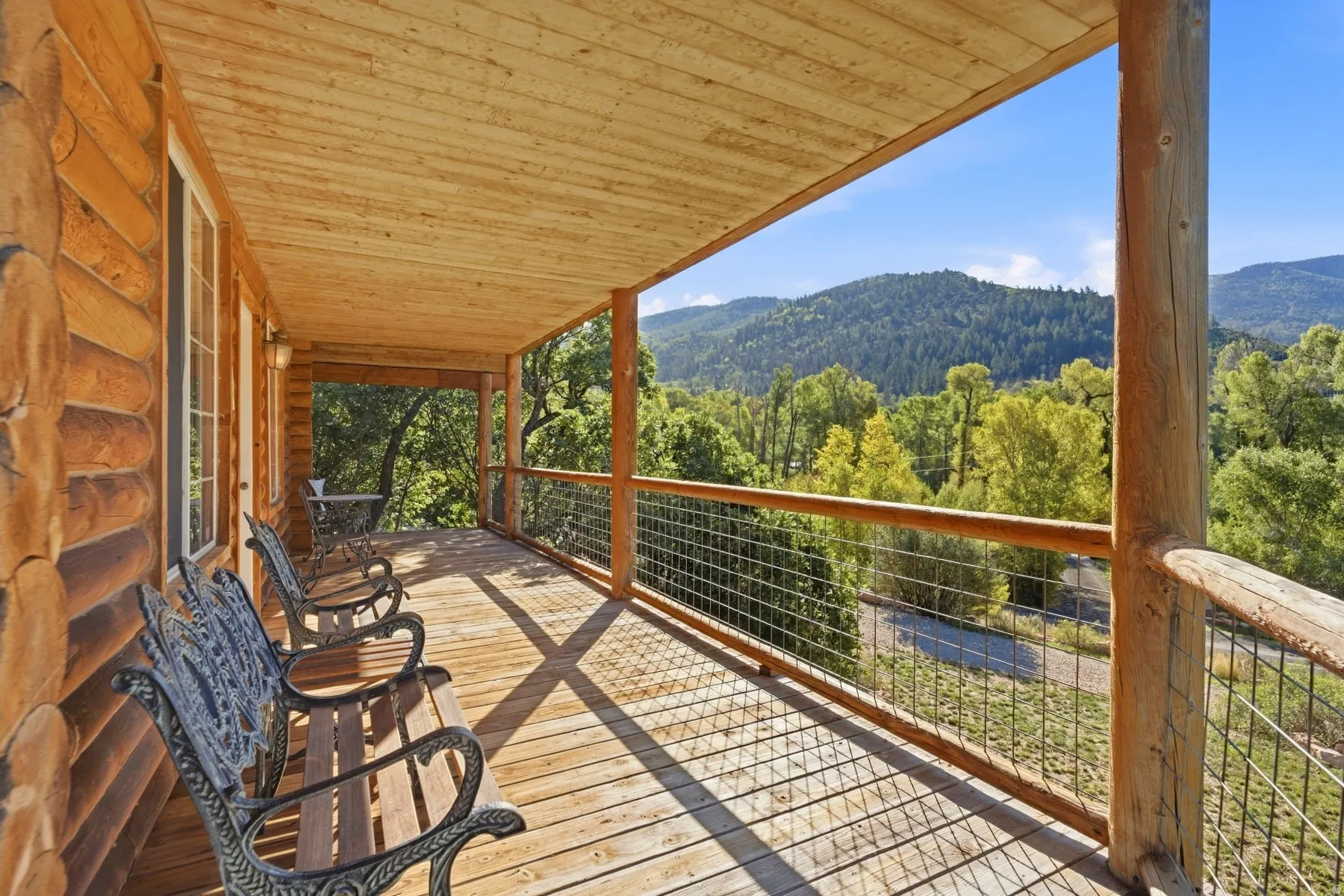 Expansive covered porch featuring wood decking, exposed log siding, and natural wood railings with wire infill