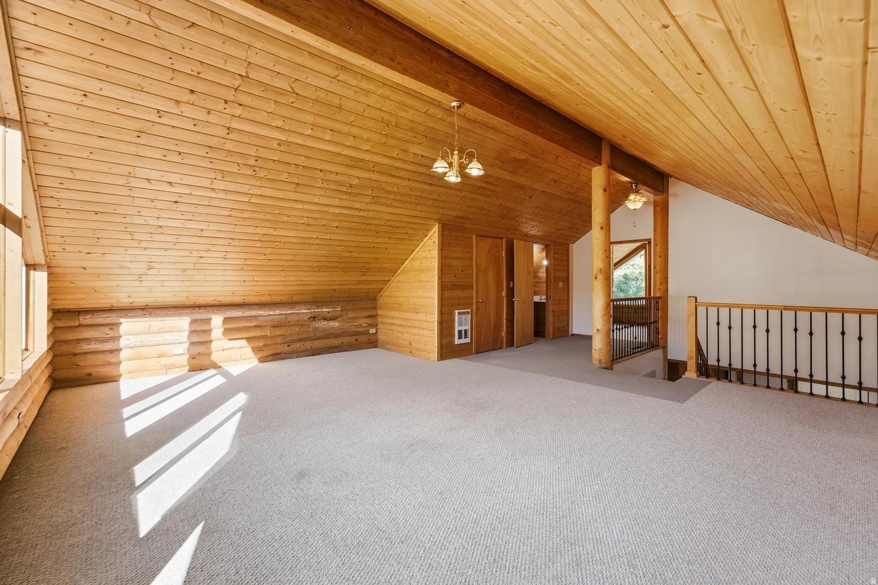 Expansive room featuring wood-paneled walls and ceiling, wall-to-wall carpeting, and a wrought iron and wood railing