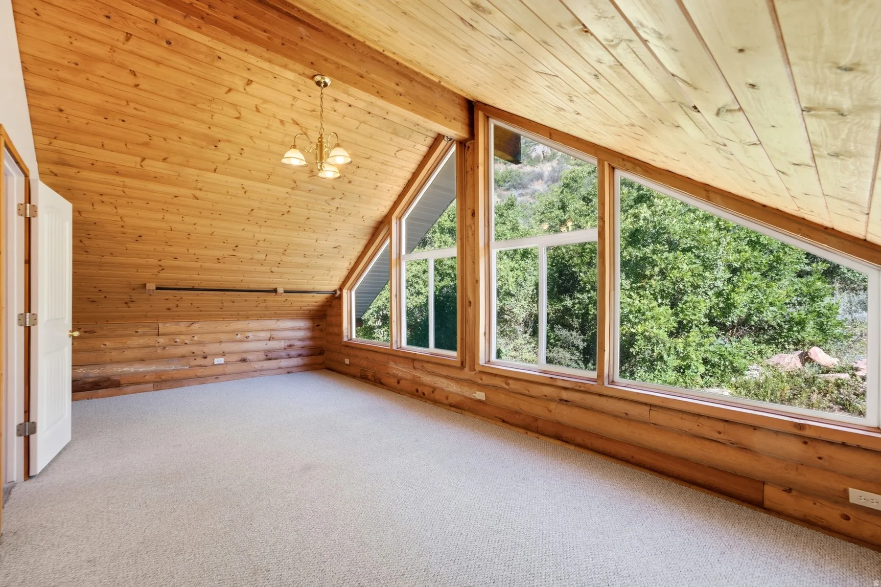 Vaulted wood-paneled ceiling, wood-plank walls, large picture windows, and light-toned carpet flooring
