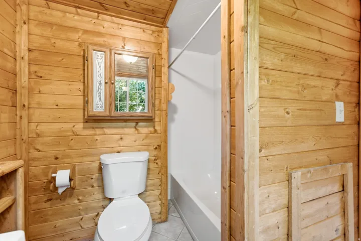 Bathroom featuring wood paneling, a white toilet, a built-in medicine cabinet with decorative glass, and a white bathtub