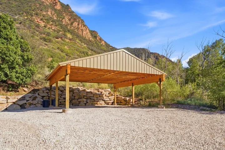 Gravel surface, covered structure, wood beam construction, metal roof, stone retaining wall, mountain backdrop