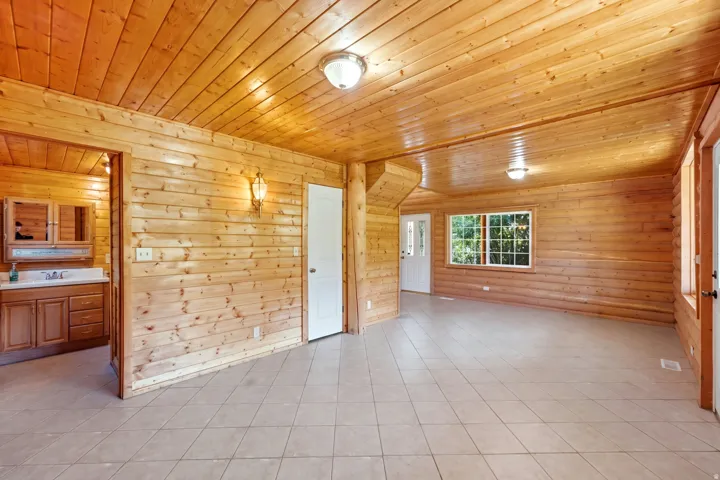 Wood-paneled walls and ceiling, recessed ceiling lighting, tile flooring, white-framed window, and a built-in bathroom vanity with an integrated sink