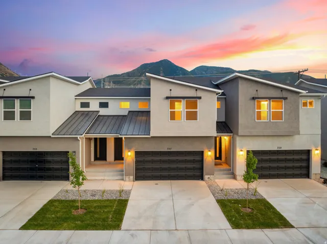 Contemporary facade featuring stucco and metal roofing, individual garage entrances, and mountain backdrop