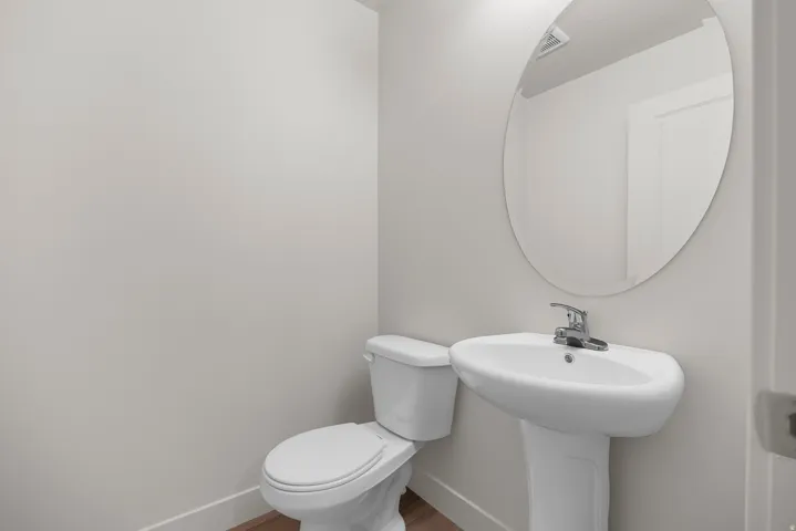 Pedestal sink with chrome faucet, oval mirror, and white toilet