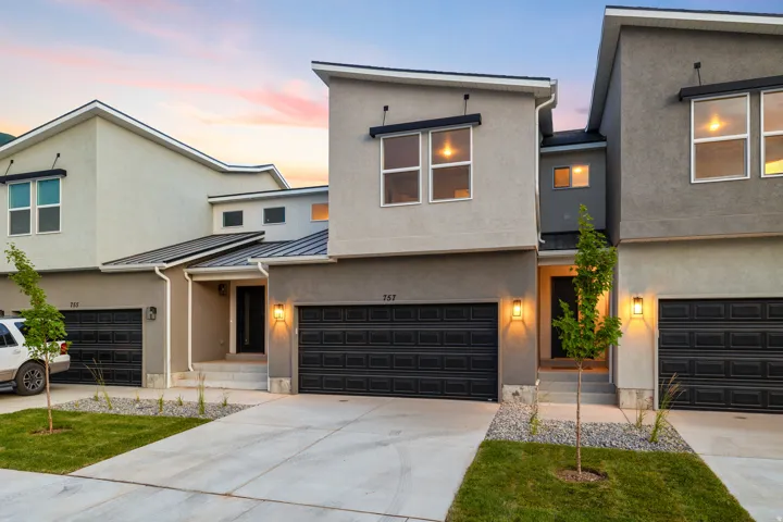 Contemporary stucco exterior with a multi-level roofline, prominent two-car garage, multiple windows, and exterior wall sconces