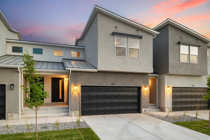 Modern stucco exterior with a prominent single-panel front door, an attached two-car garage, and a metal roof accent